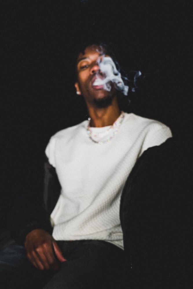 Person in white sweater exhaling smoke against dark background.