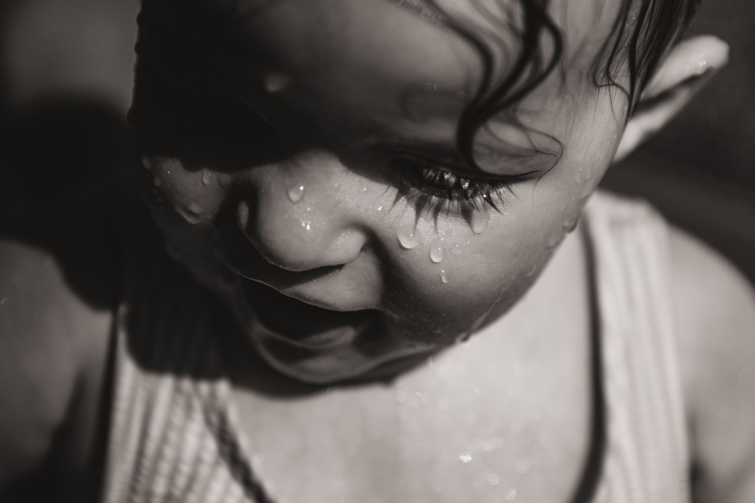 Close-up black and white portrait of a wet child with water droplets on their face.