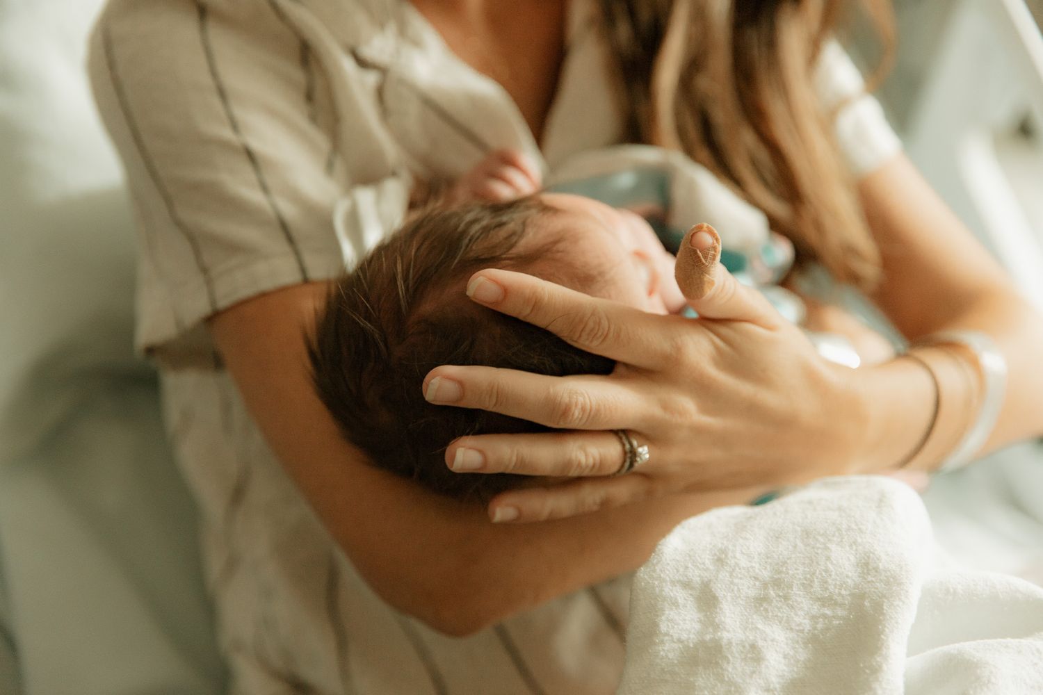 A new mother gently cradles her newborn baby's head in her hand at the hospital.