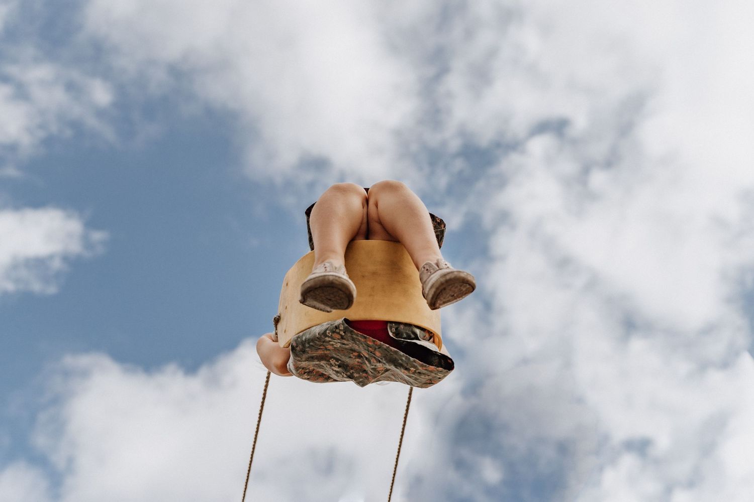 Low angle view of feet in boots swinging against blue cloudy sky.