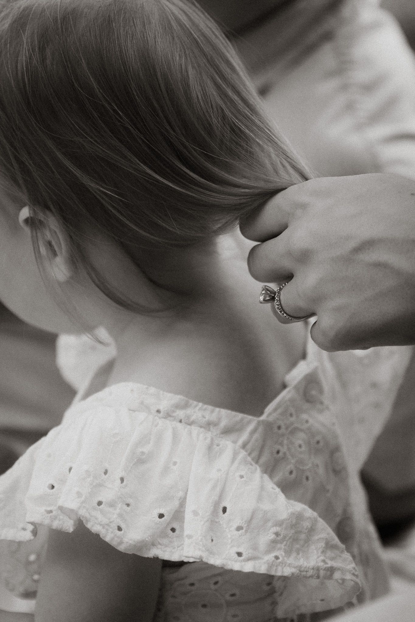 A parent with a ring gently styles a young girl's hair in this black and white close-up photo.