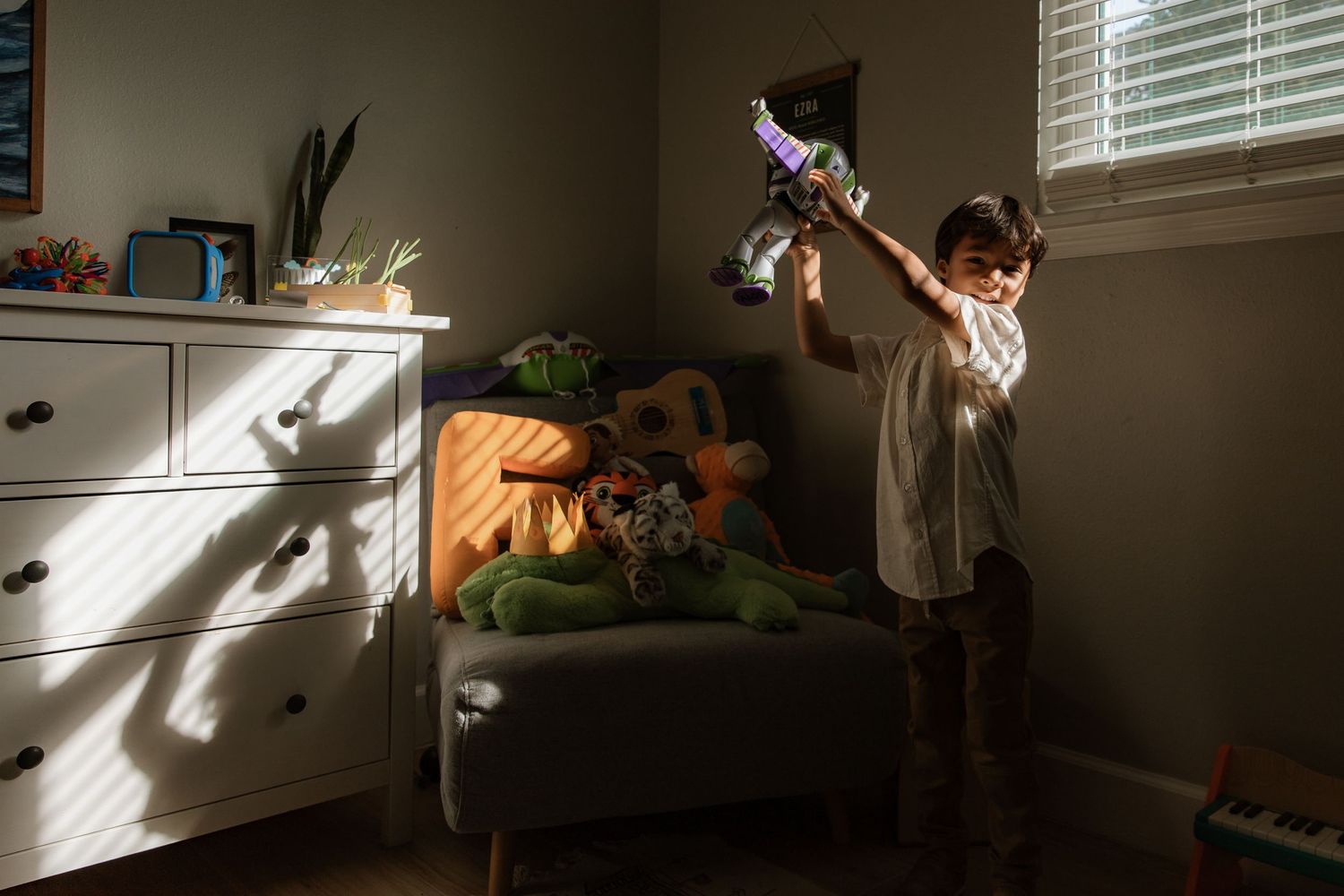 Child playing with a colorful toy in a sunlit bedroom, raising it above their head near a window.