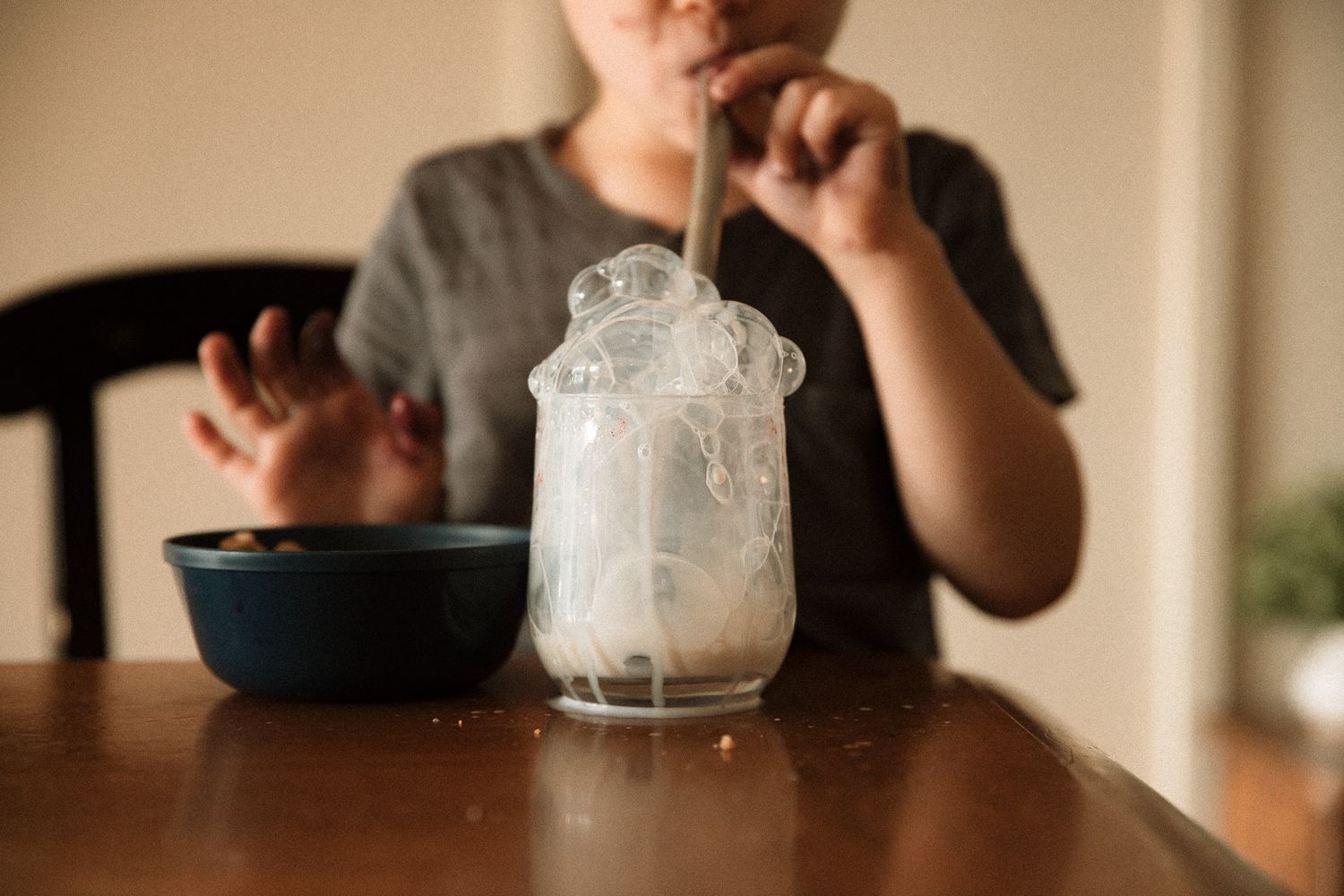 A child sits at a wooden table stirring a fizzing science experiment in a glass.