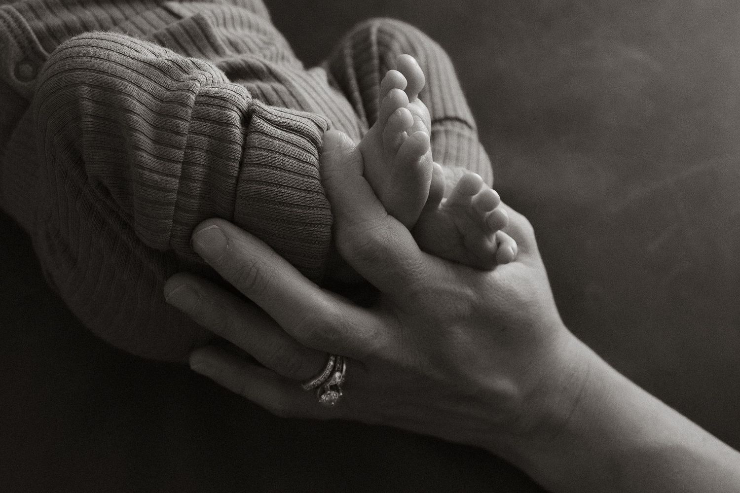 Black and white close-up of a parents hands tenderly holding tiny newborn baby feet.