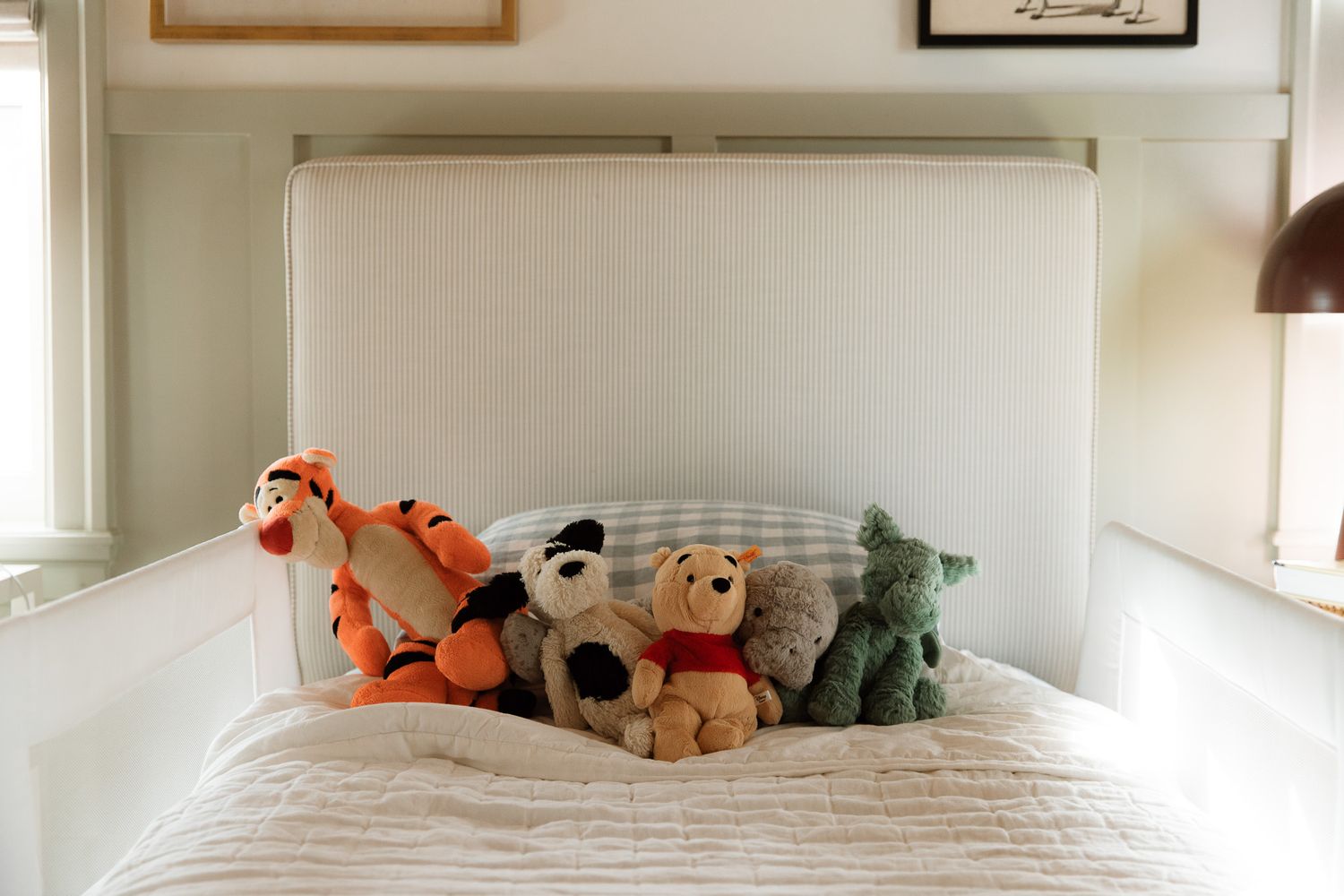 Collection of stuffed animals including Tigger and Winnie the Pooh arranged on white bed in a family home in Maitland, Florida.