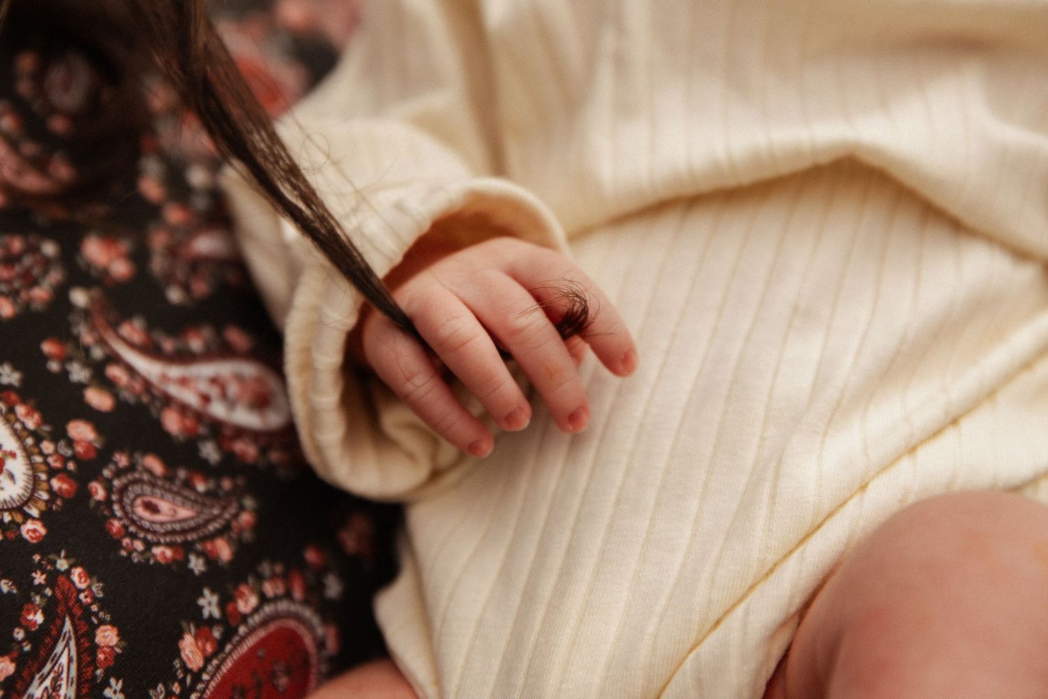 Close-up of newborn baby hand resting on cream textured blanket.