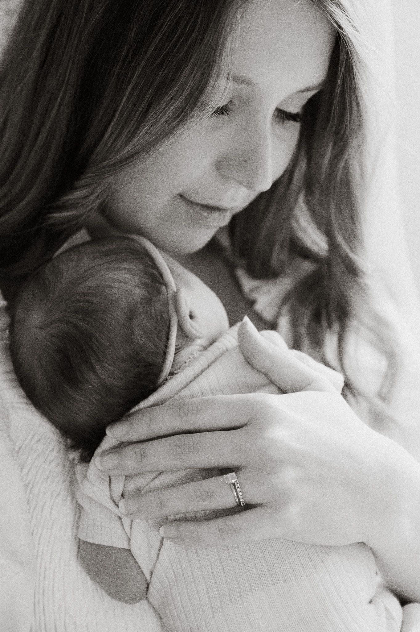 Black and white portrait of mother gently cradling sleeping newborn baby close to her chest.