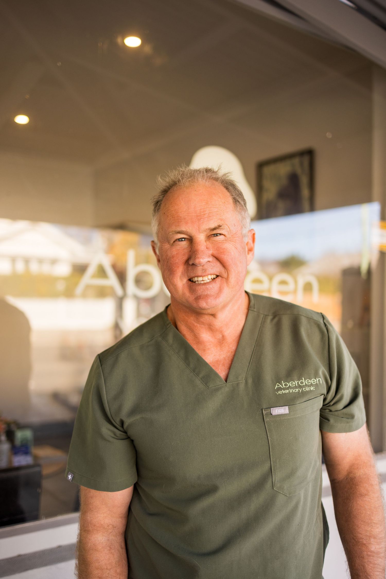 Smiling male veterinarian in green Aberdeen Veterinary Clinic scrubs standing outside the clinic entrance.