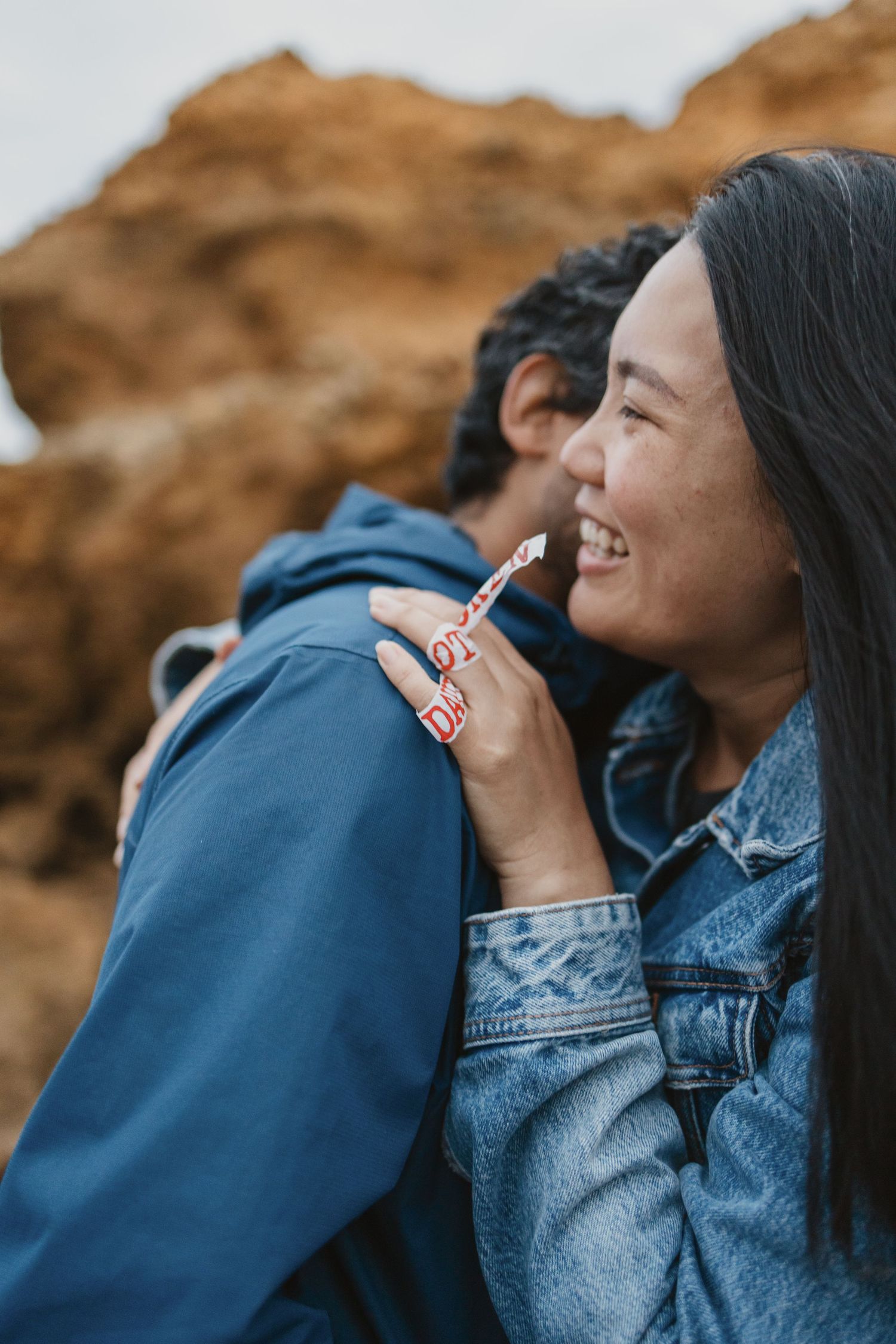 Happy couple embracing and smiling together against rocky outdoor background.