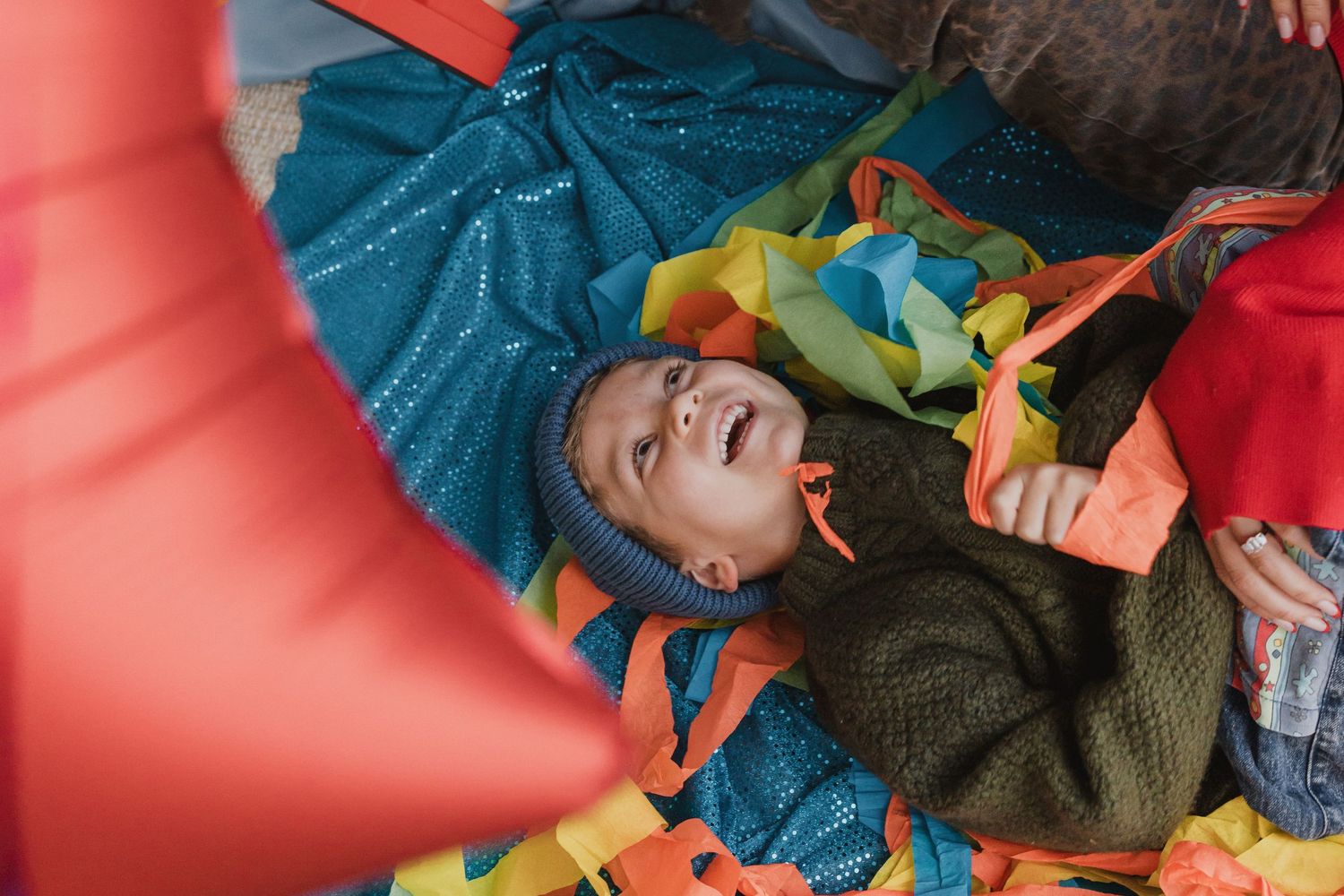 Toddler laughing while lying on a colourful pile of streamers and balloons at a first birthday photoshoot in a Geelong studio.