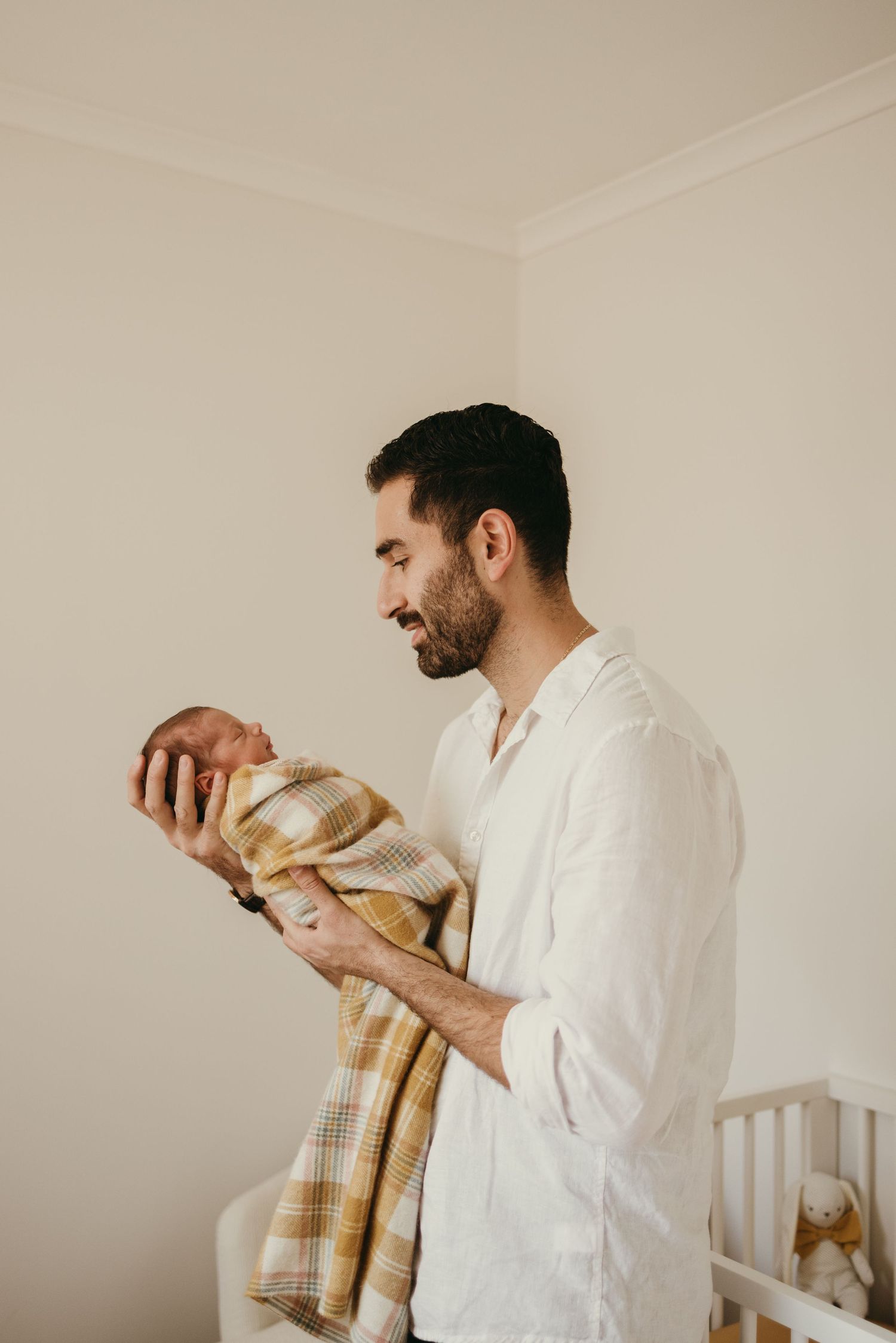 Parent in white shirt holding a baby wrapped in plaid blanket in a nursery setting.