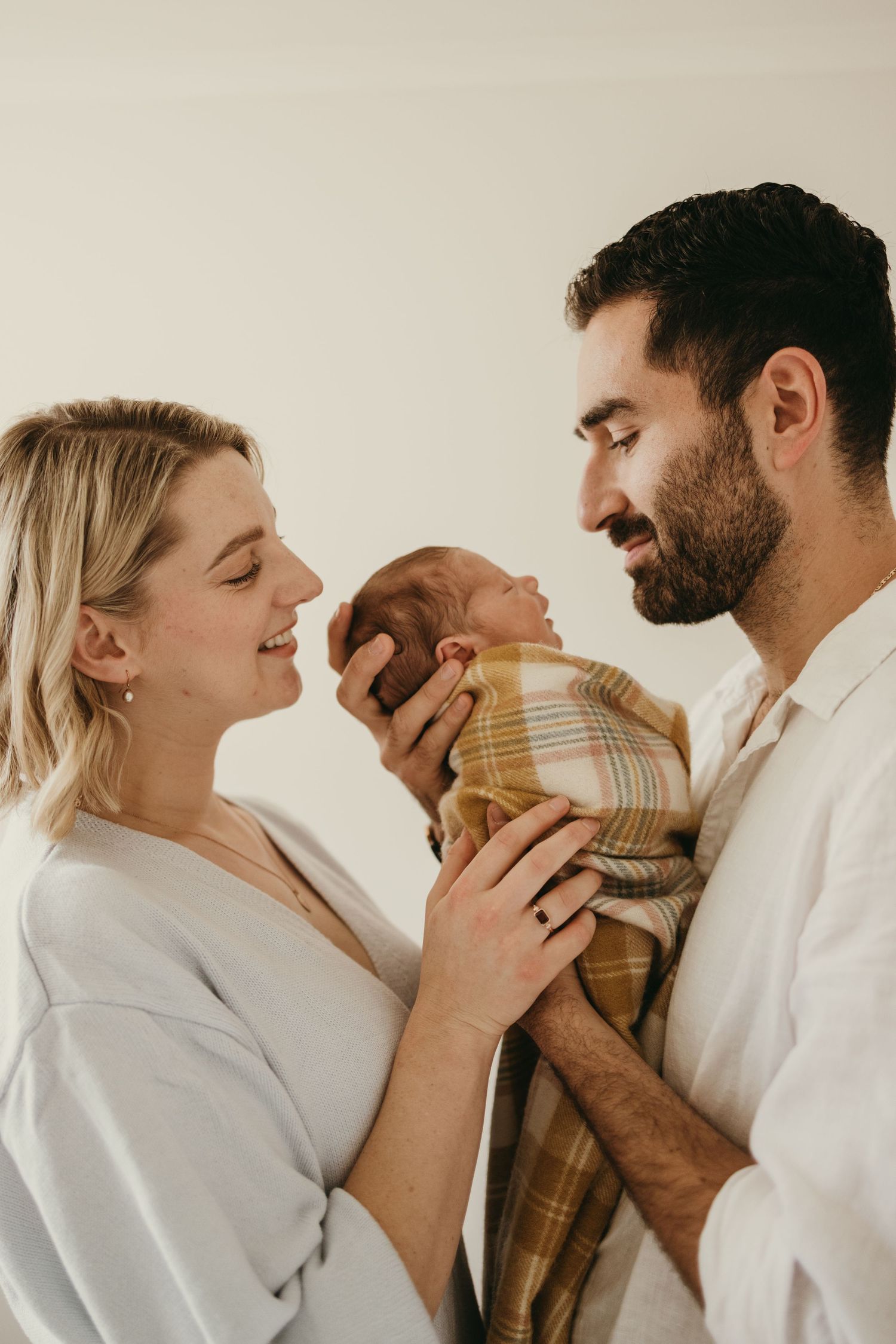 Parents sharing a loving moment with their newborn wrapped in a plaid blanket.