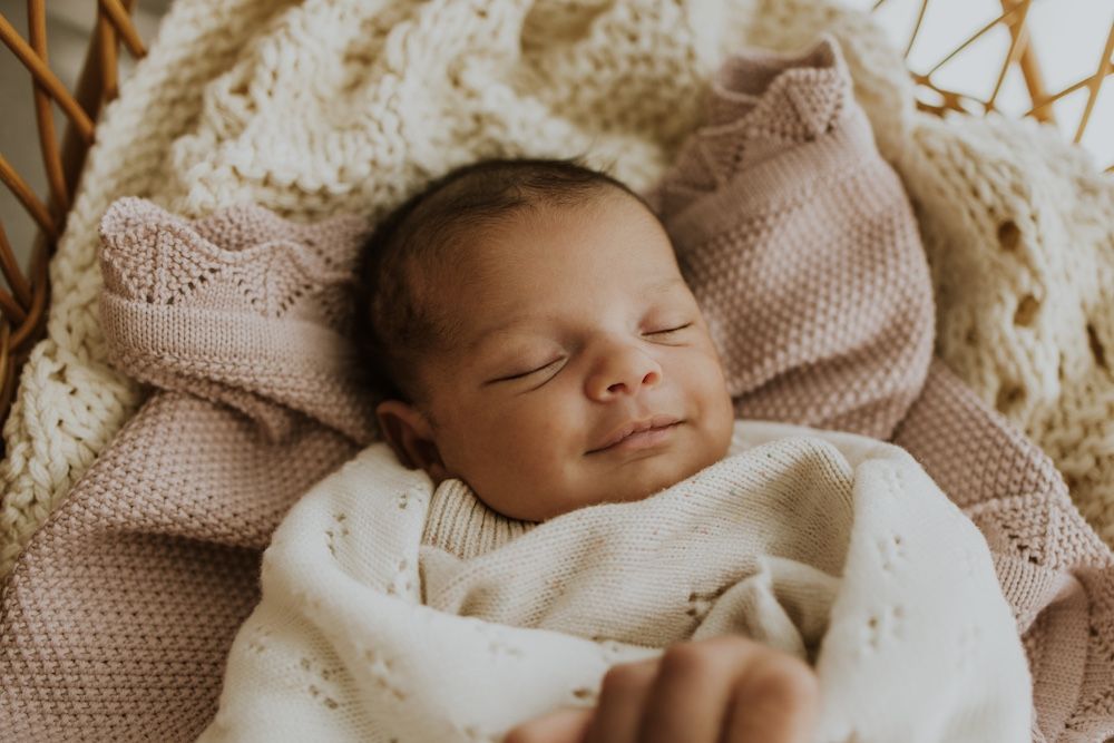Peaceful sleeping newborn wrapped in cream knit blankets.