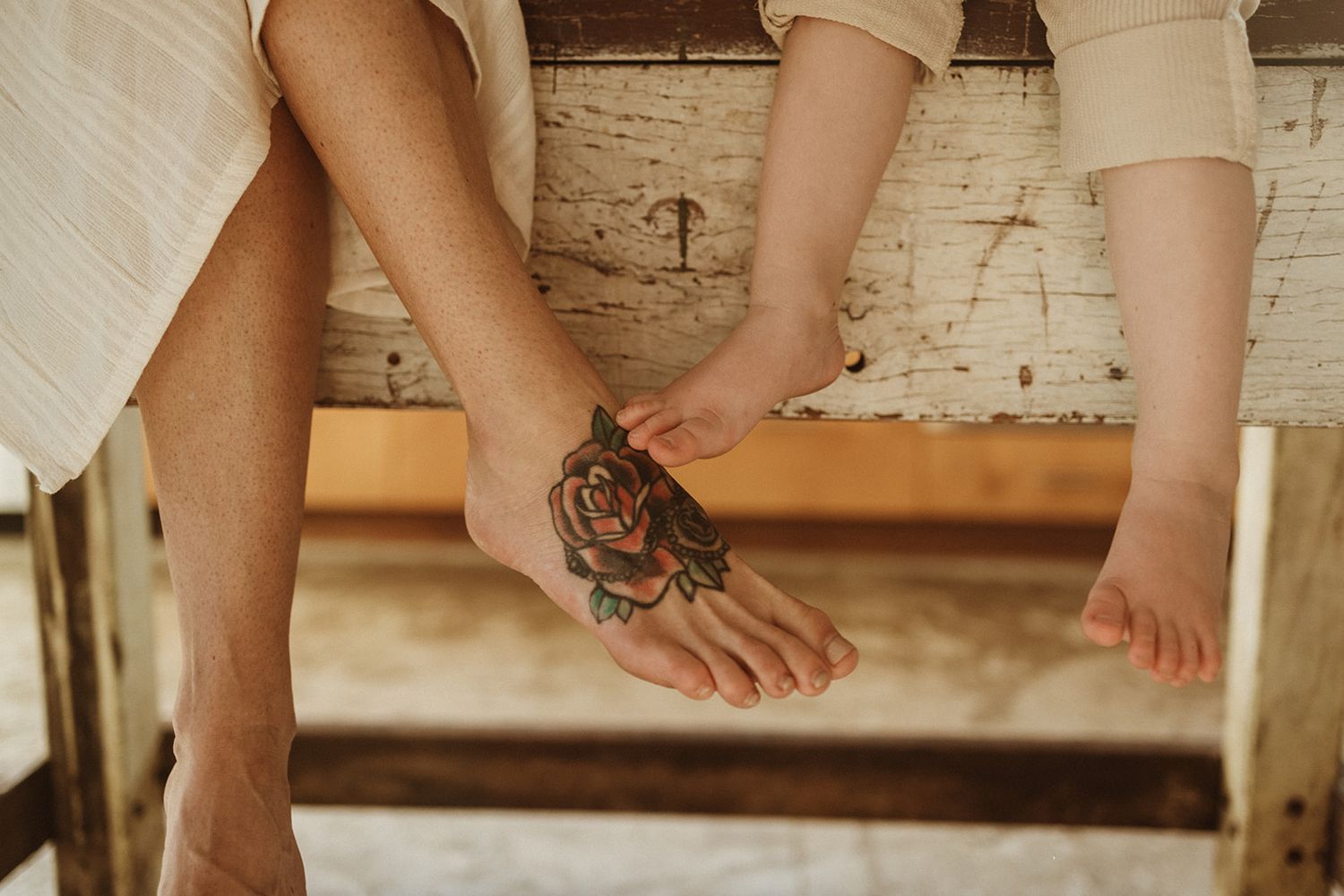 Close-up of feet on wooden steps showing contrasting sizes and a decorative tiger tattoo.