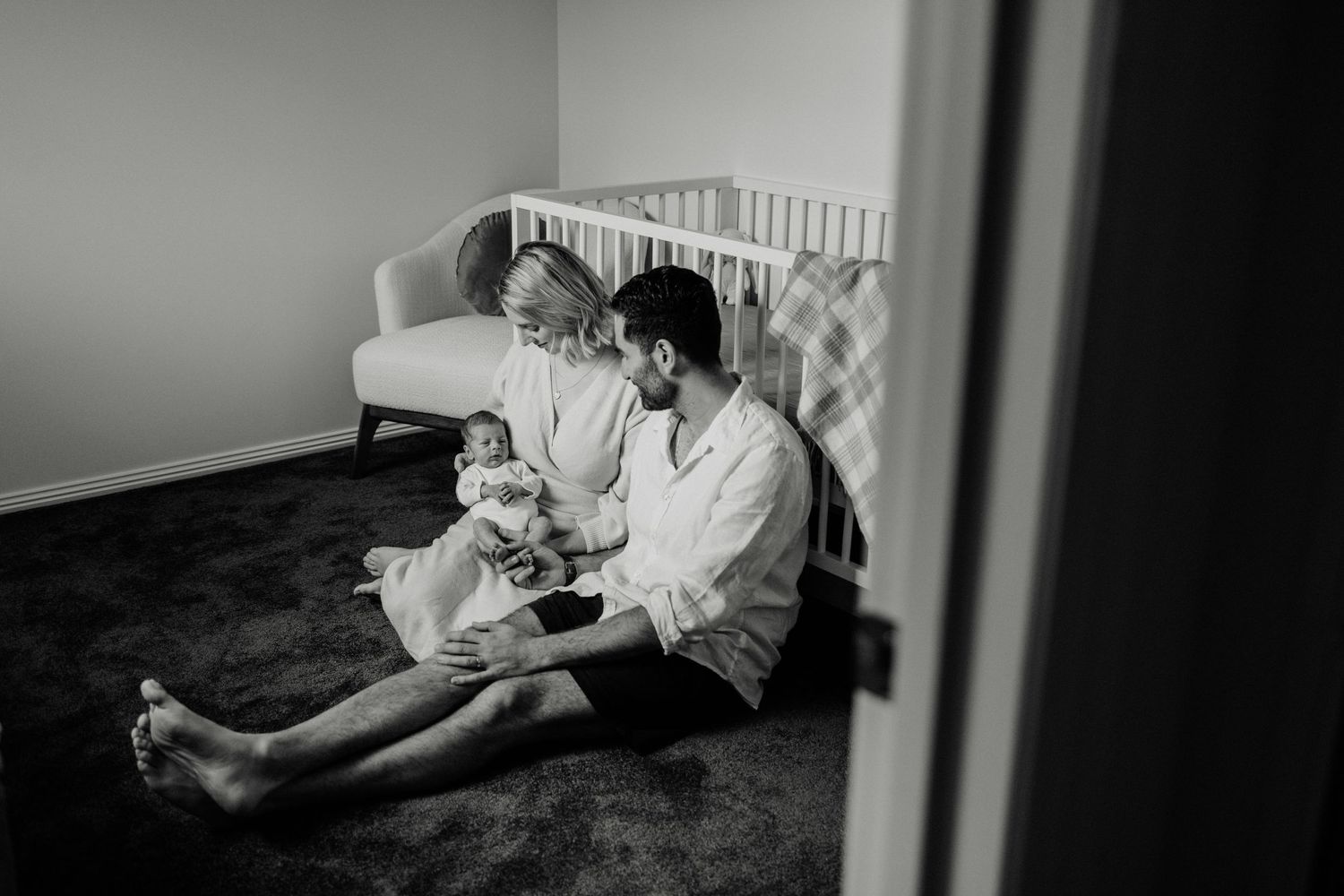 Black and white photograph of tender family moment in nursery corner.