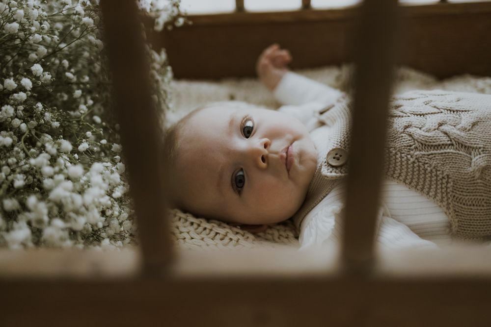 Baby lying in crib viewed through slats in soft vintage-style photography.