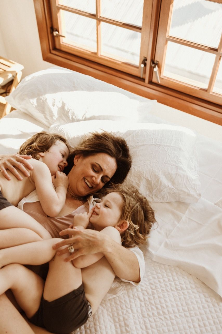Family cuddle time on white bed with morning light streaming through window.