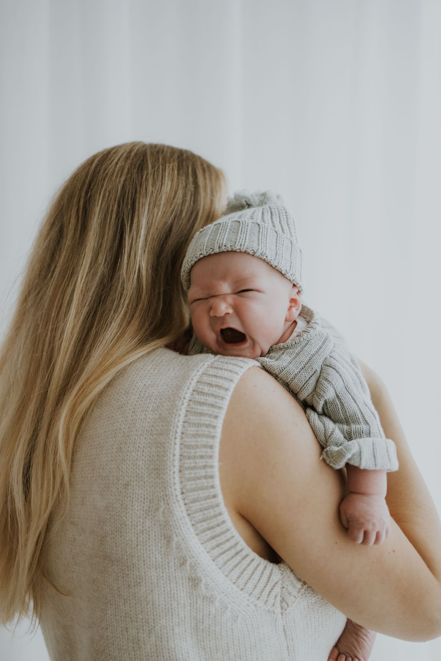 Baby in knit outfit yawning while being held over shoulder.