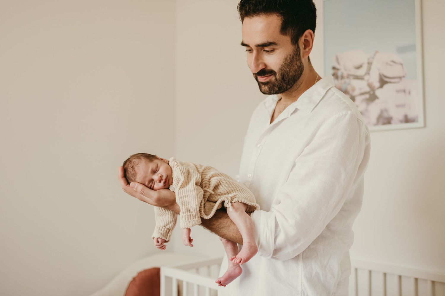 Parent in a white shirt gently holding a newborn baby in a soft, natural light nursery.