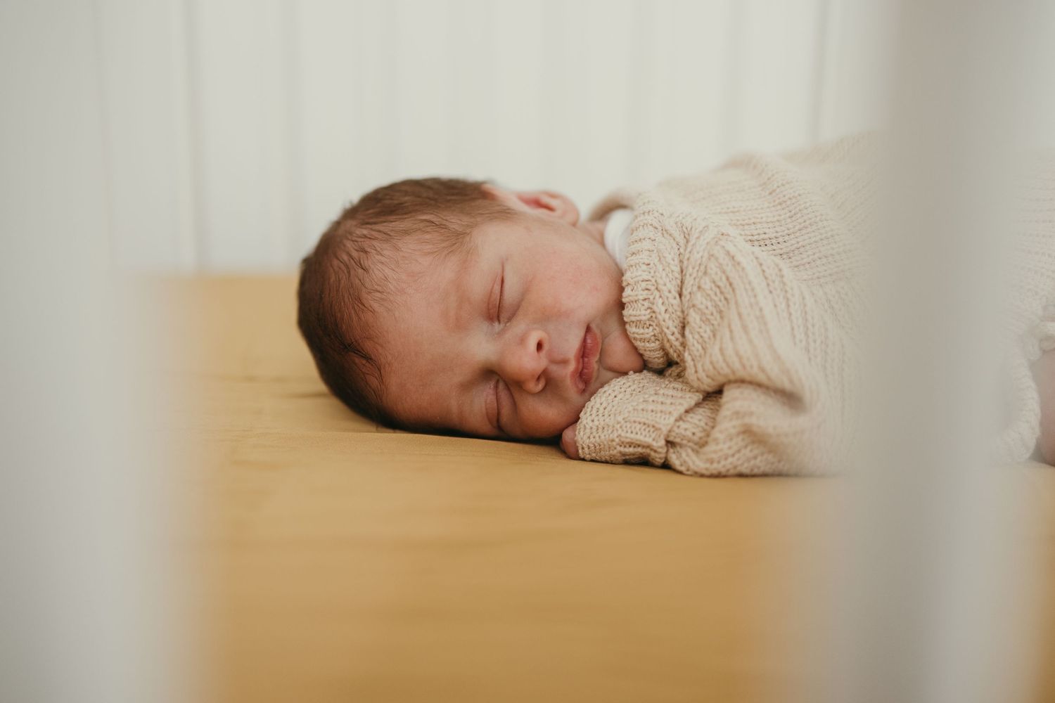 Peaceful newborn sleeping on wooden surface in soft beige sweater.