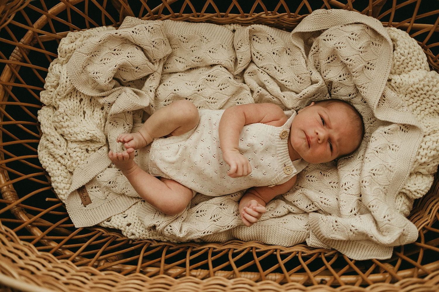 Newborn baby sleeping peacefully in a wicker basket lined with a soft cream knit blanket.