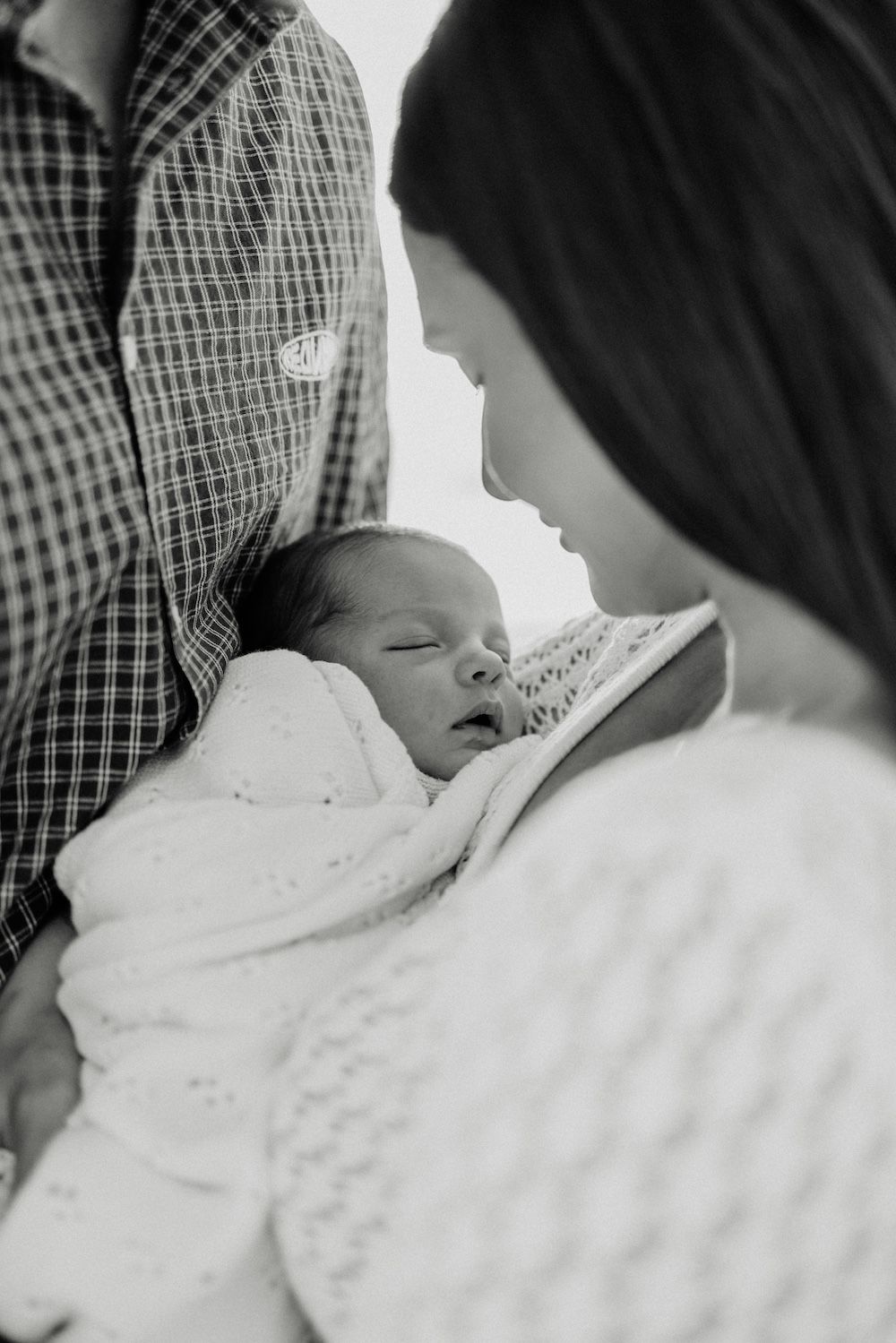 Black and white image of a sleeping newborn being held while parents gaze lovingly. Geelong Melbourne newborn maternity family motherhood