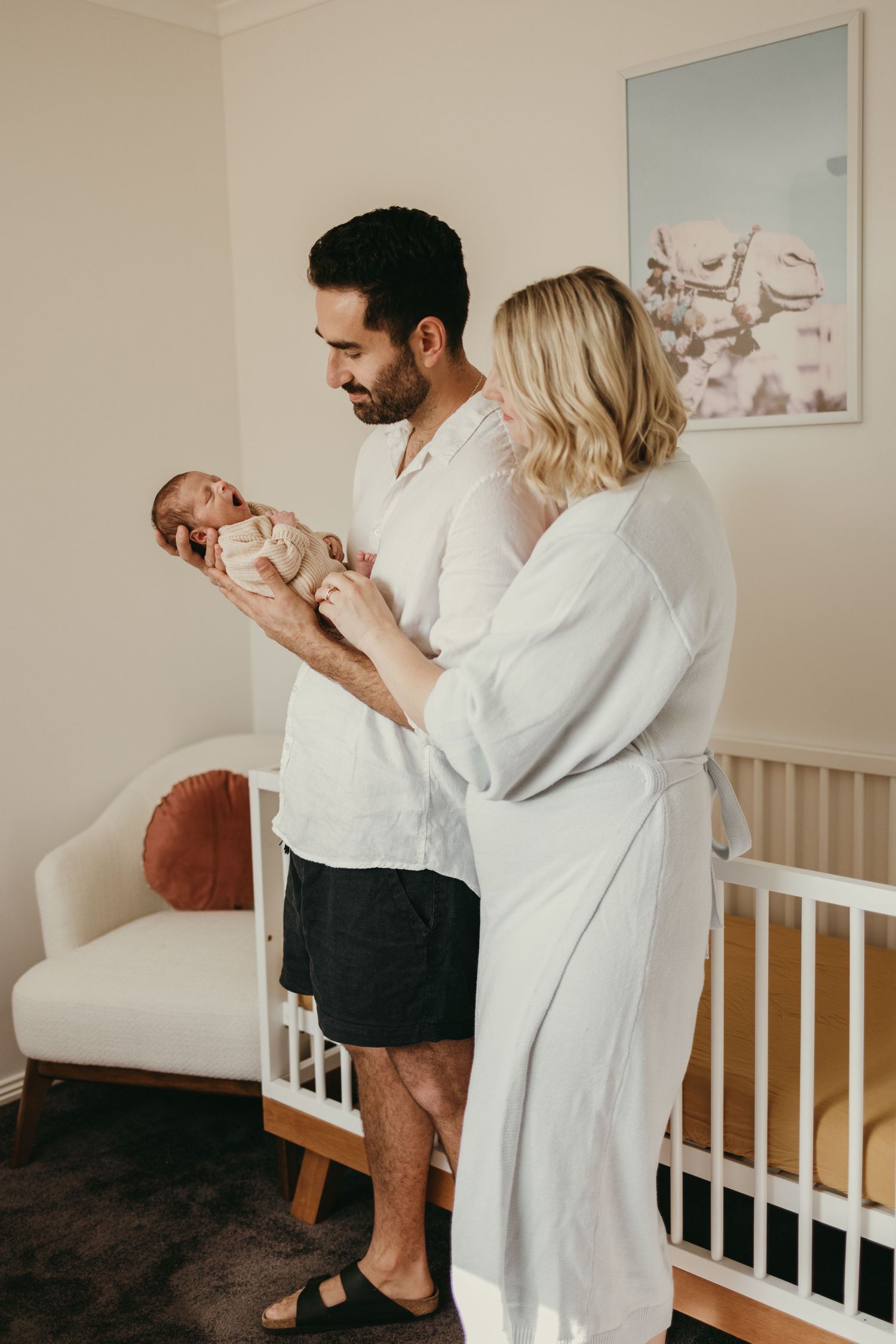 A tender moment in a nursery as new parents hold their newborn baby together near a white crib.