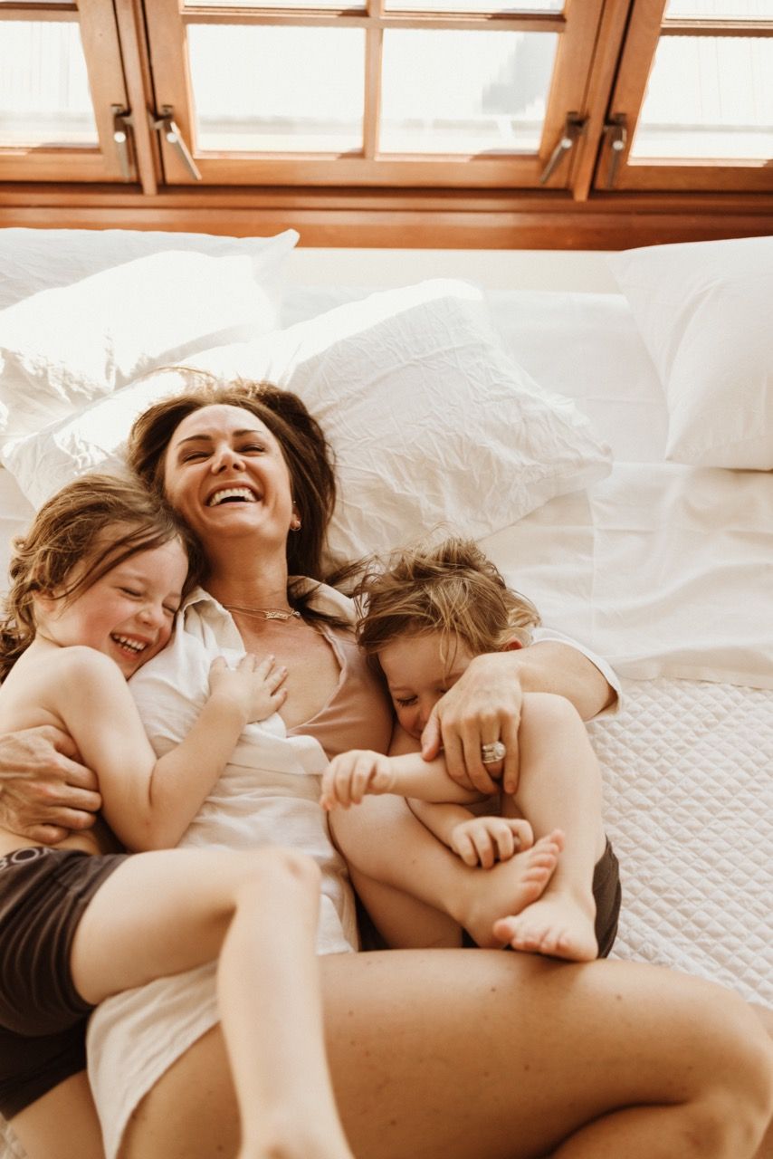 Joyful cuddles and laughter shared on a cozy bed near sunlit windows.
