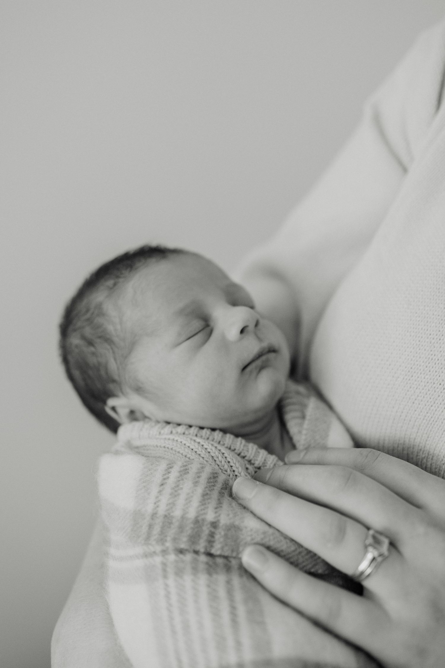 Black and white portrait of peaceful sleeping newborn swaddled against caregiver.