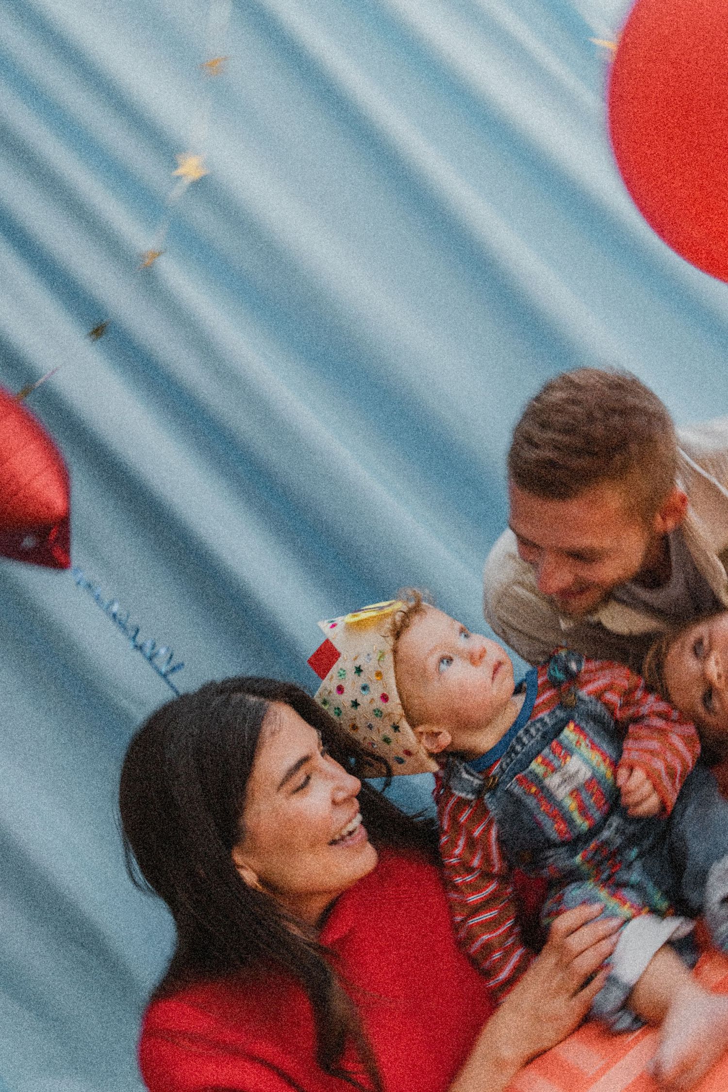 Happy family with two parents and a toddler celebrating with red balloons outdoors.