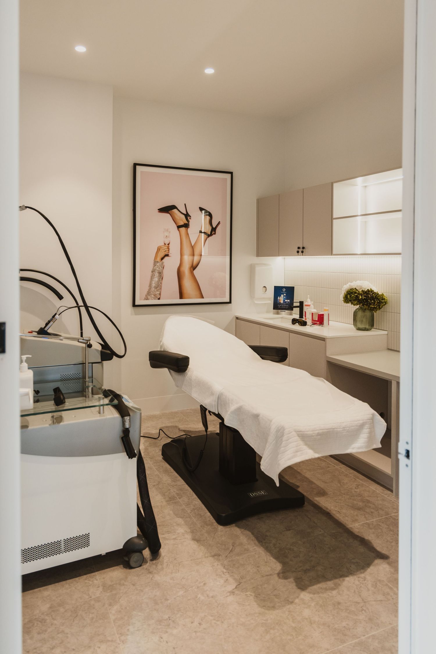 Modern medical spa treatment room with adjustable table, laser equipment, built-in cabinetry, and elegant wall art.