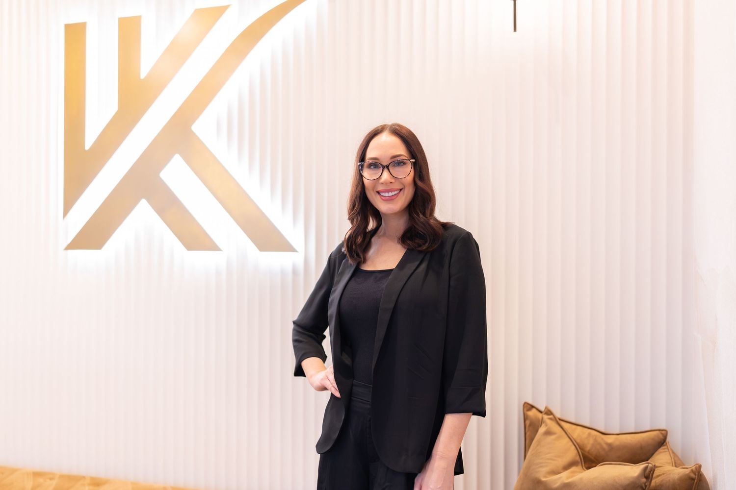 Professional woman in black blazer smiling confidently in front of a modern gold letter K logo backdrop.