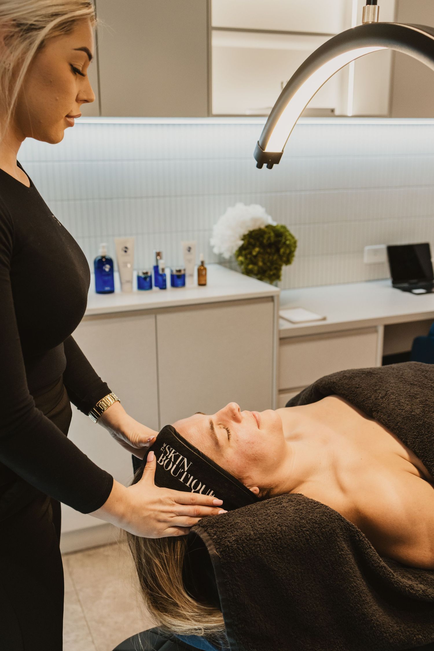 Esthetician applying a Skin Boutique headband to a client lying on a treatment bed in a modern spa.