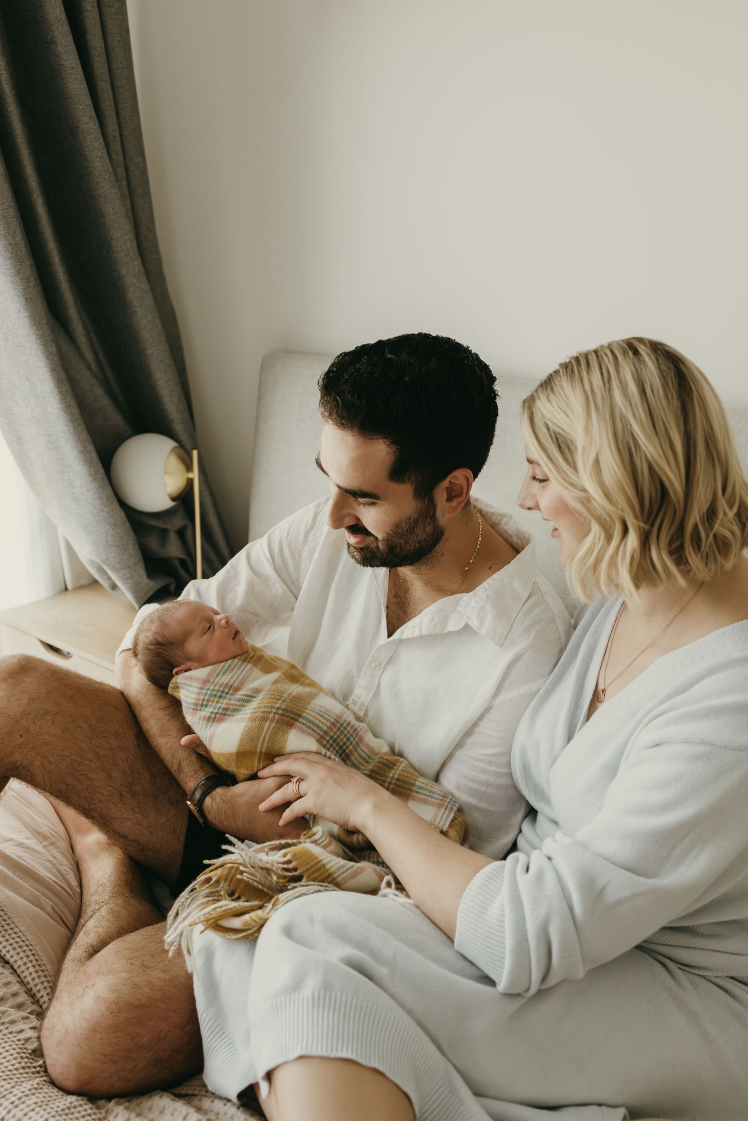 New parents lovingly hold their newborn baby while relaxing together on a cozy bed.