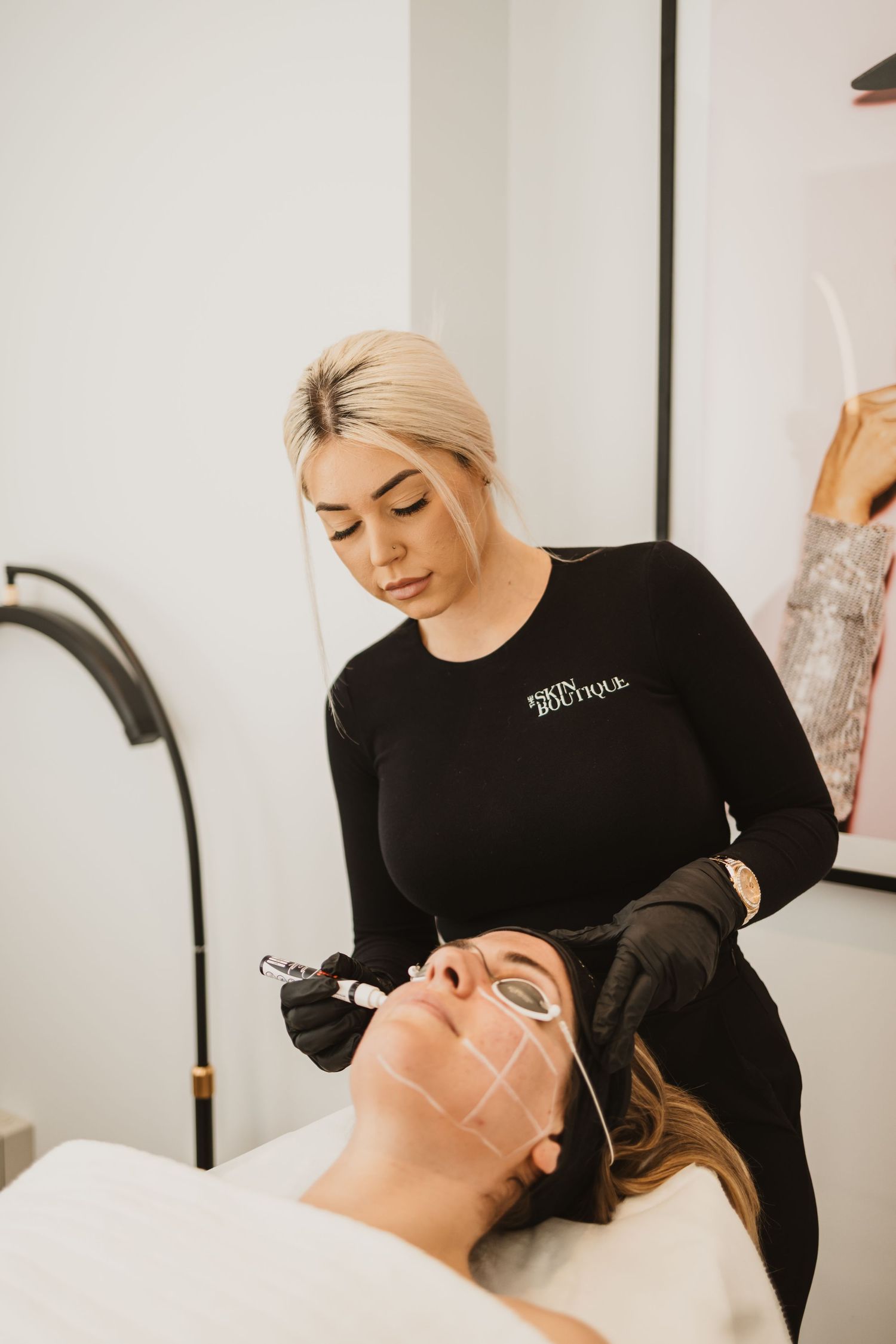 Esthetician in black uniform performing a facial treatment on a client at a beauty boutique spa.