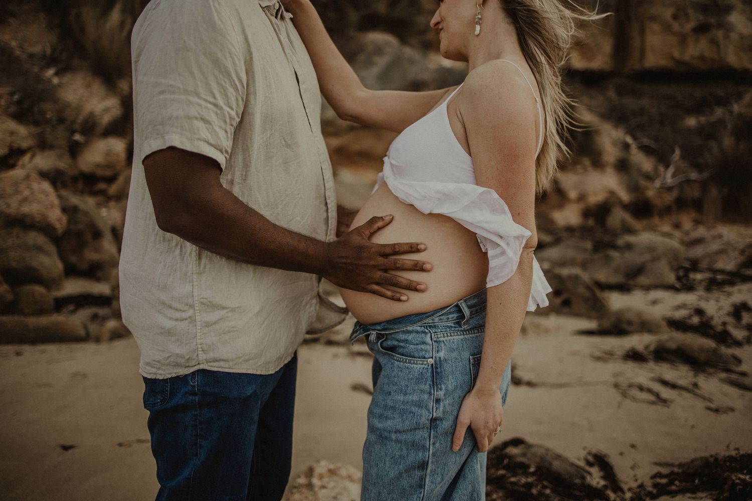 Geelong maternity photography - pregnant couple on the beach, partner holding her baby bump.