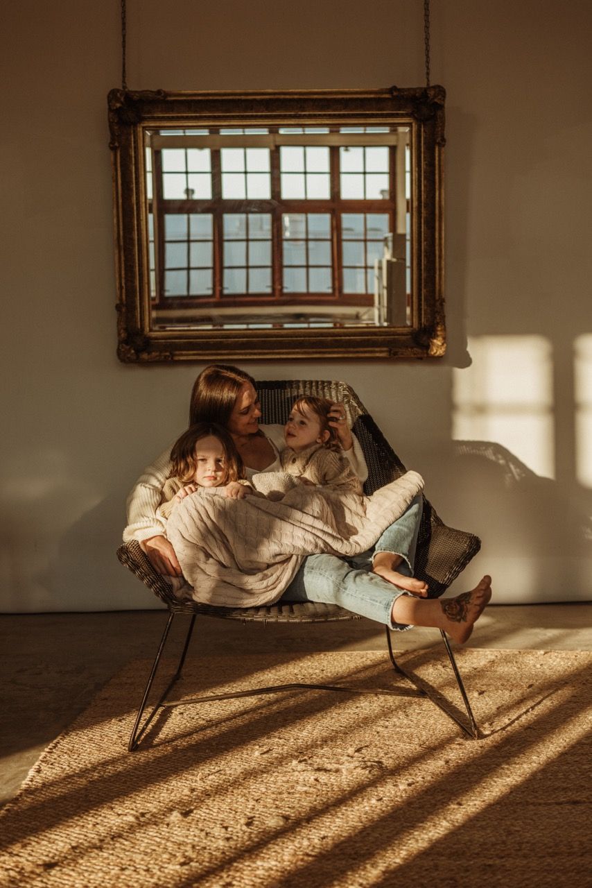 Family relaxing together in a vintage chair beneath a framed window with warm afternoon light.