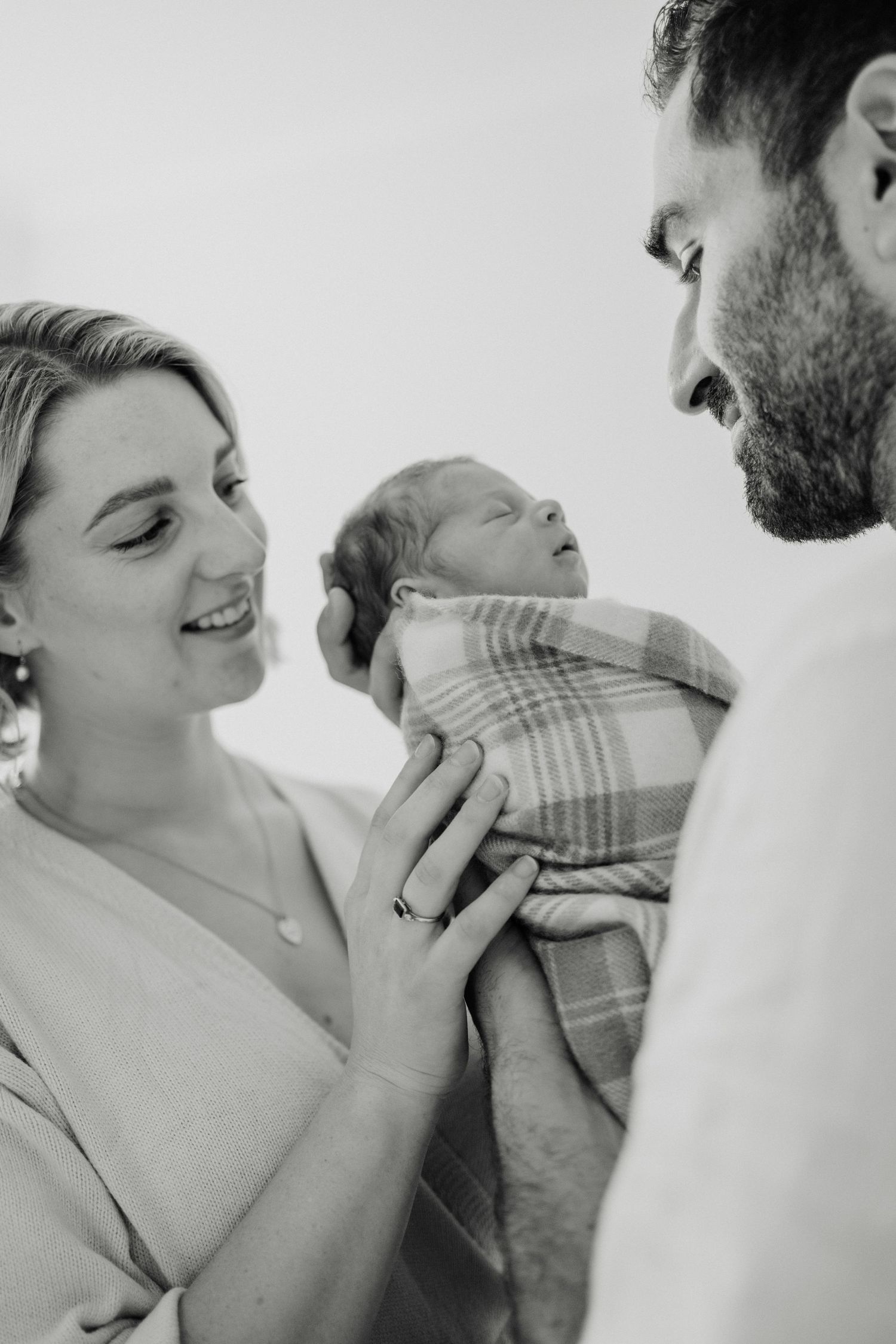 Black and white portrait of parents gazing lovingly at their swaddled newborn.