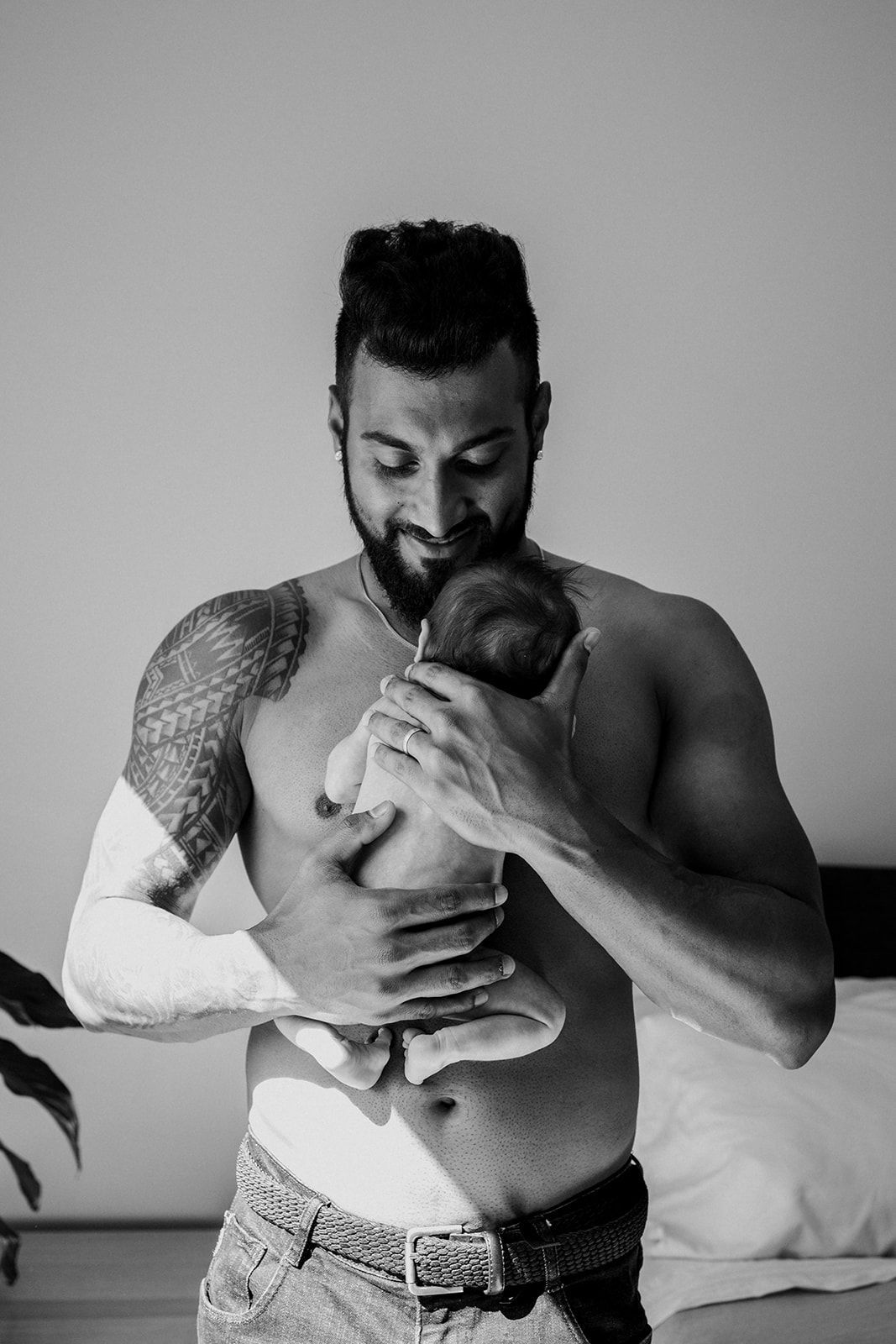 Father tenderly holding and kissing his newborn baby in a black and white at home newborn photo.