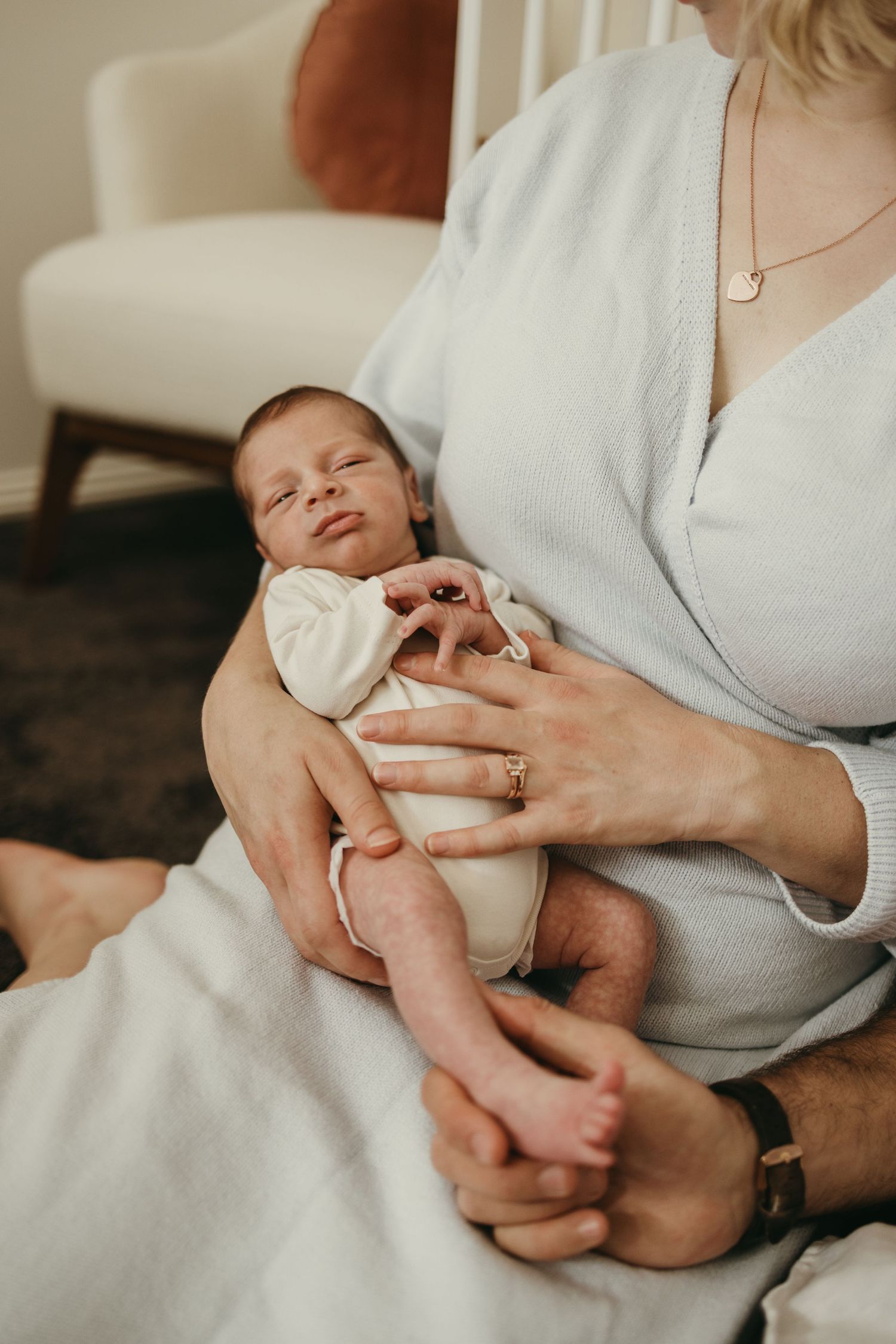 Sleeping newborn baby in white onesie cradled in parent's lap.