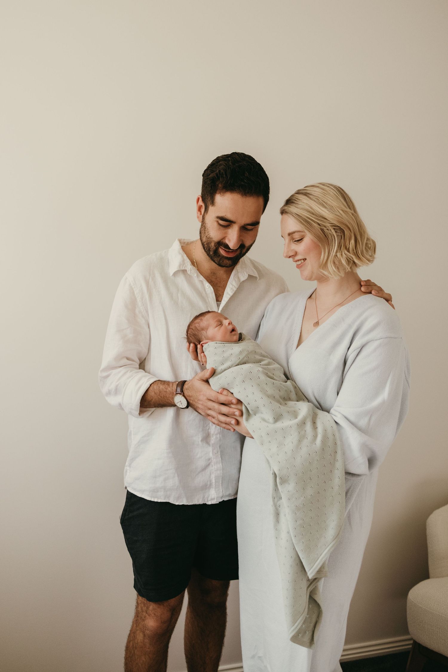 Intimate family portrait in a nursery with parents sharing a tender moment with their swaddled newborn.