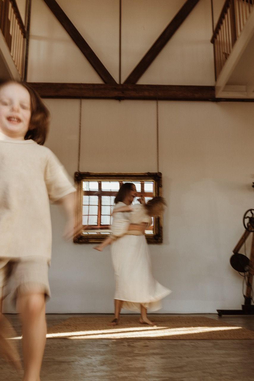 Motion-blurred scene of dancing figures in a rustic room with wooden beams and natural light.