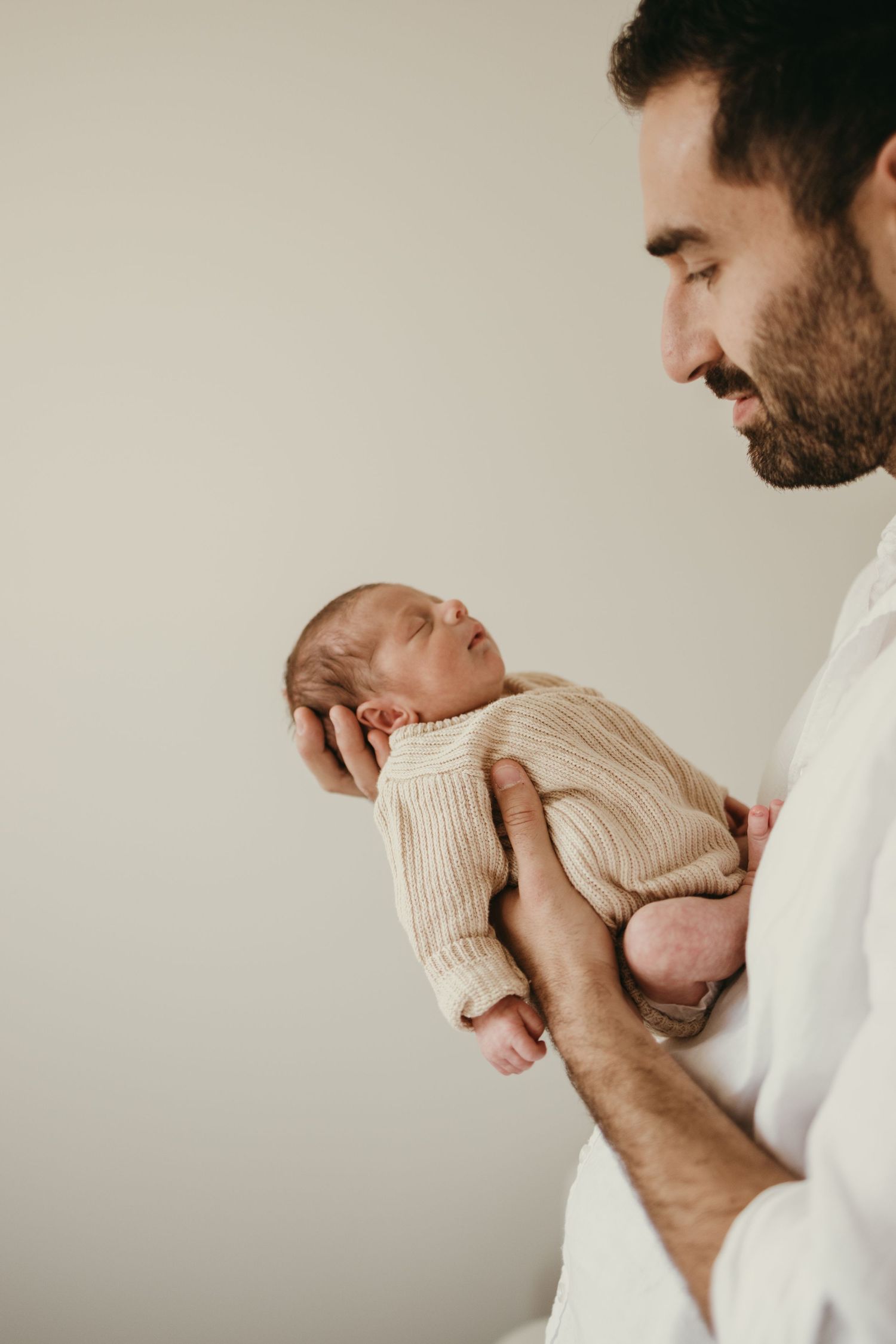 Side profile of parent holding a sleeping newborn dressed in a cream sweater.