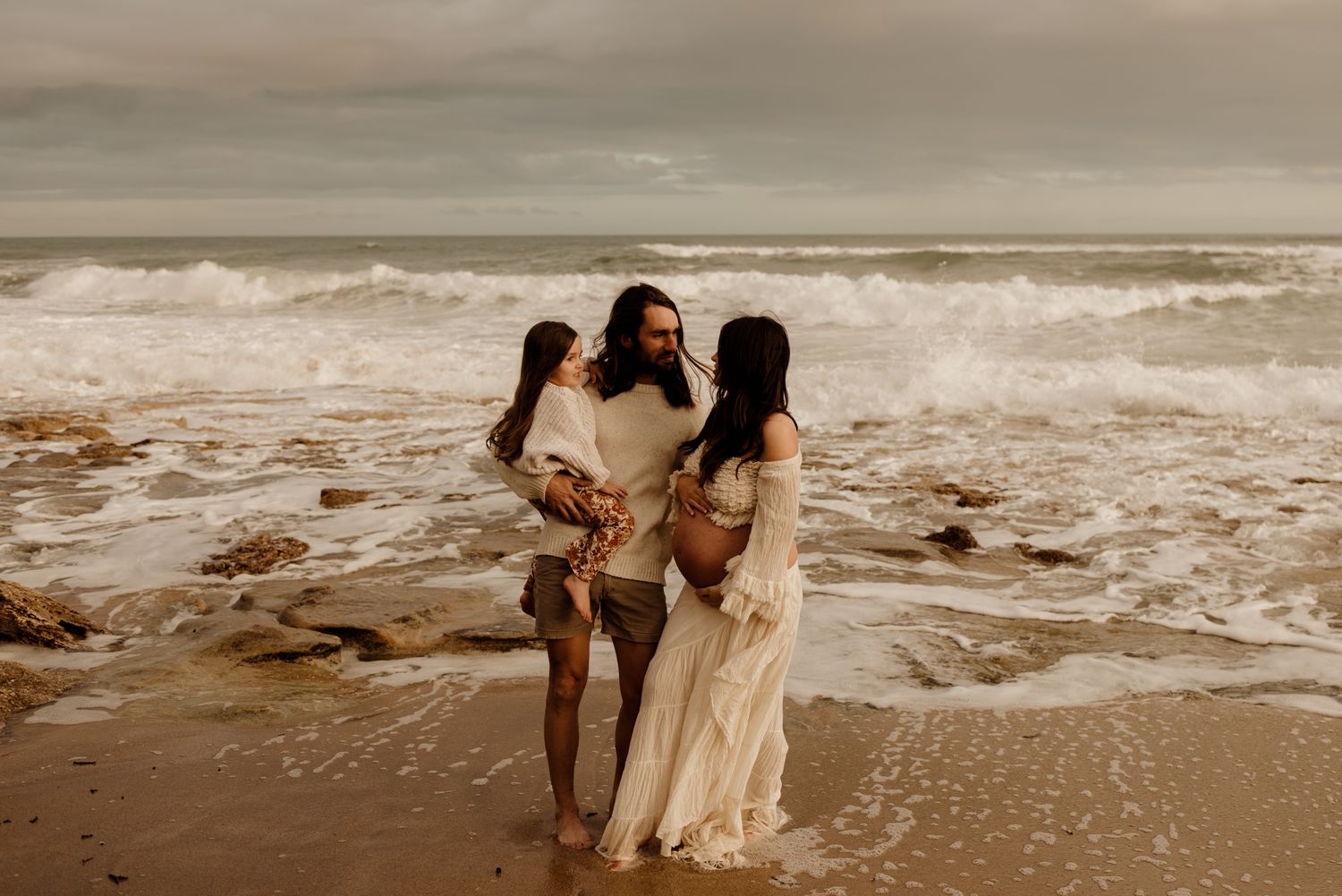 Romantic beach scene with crashing waves and moody sky at sunset.
