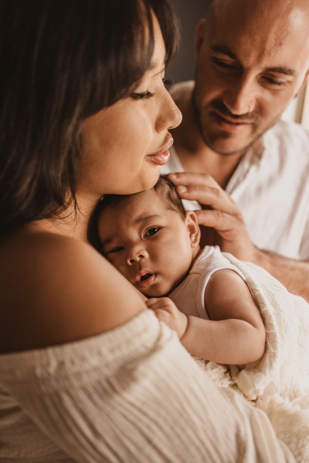 A tender family moment as parents lovingly cradle their newborn baby in warm, soft light.