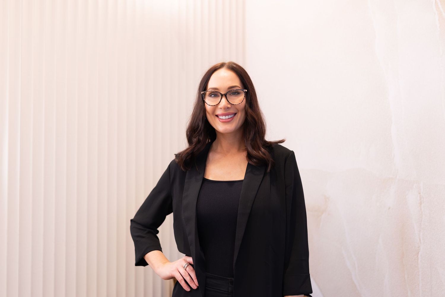 Professional woman in black blazer and glasses smiling confidently against a white background.