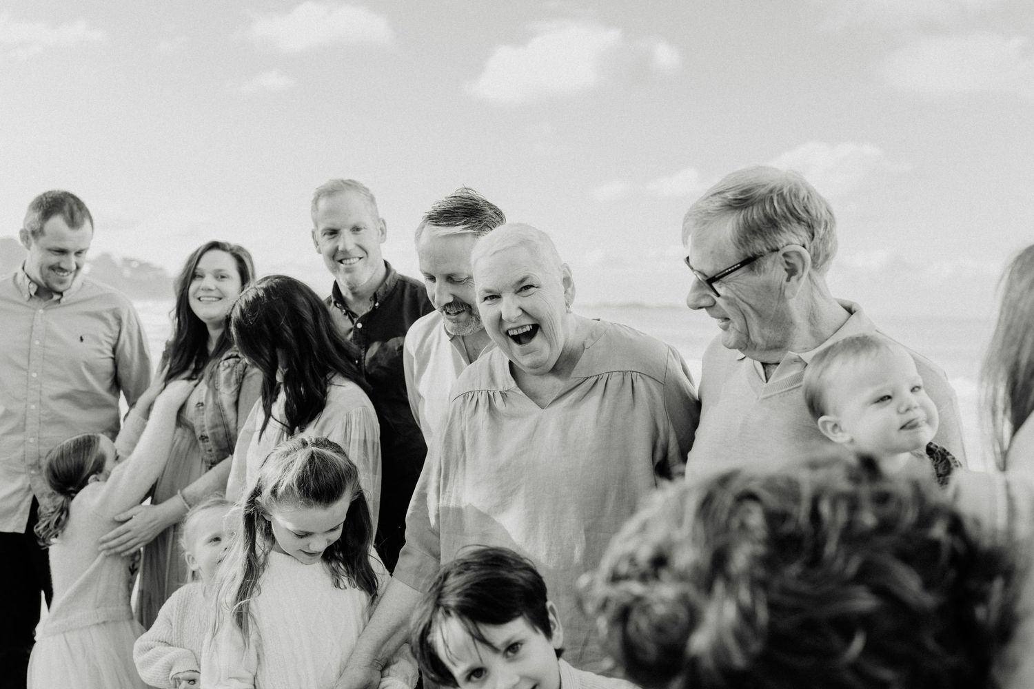Black and white family photo of multi-generational group laughing together outdoors at a beach gathering.