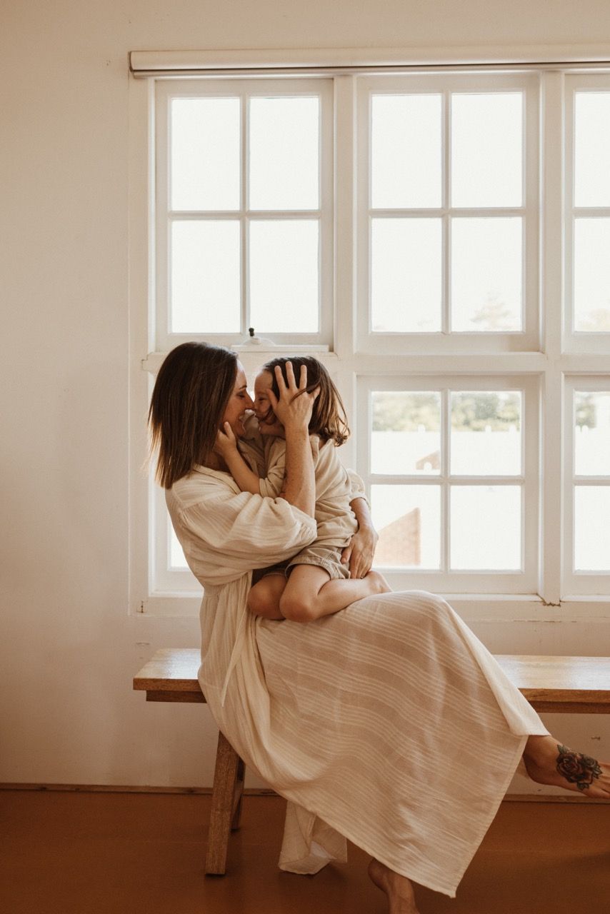 Intimate parenting moment by window seat in warm natural light.