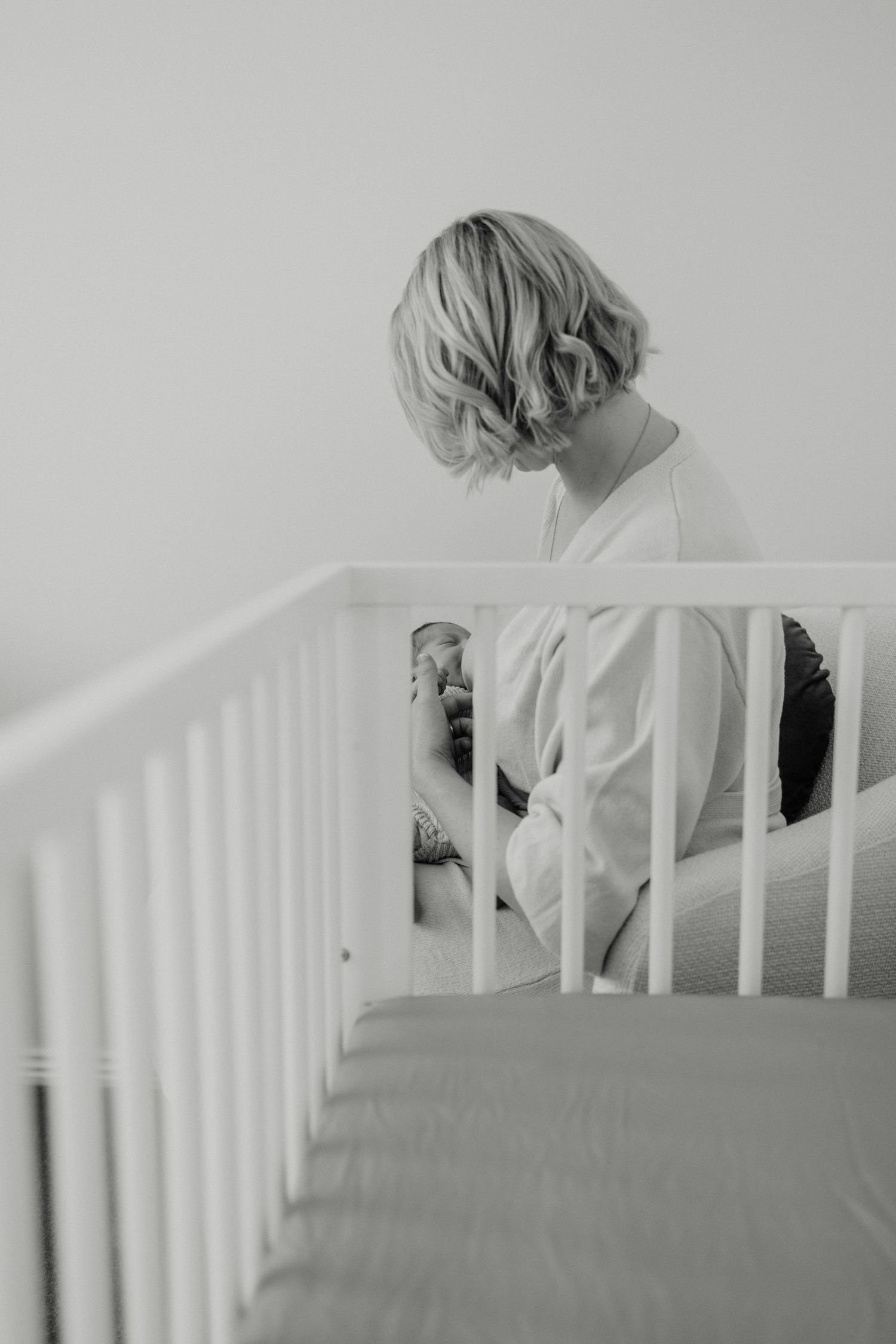 Parent leaning over white crib to check on sleeping baby.