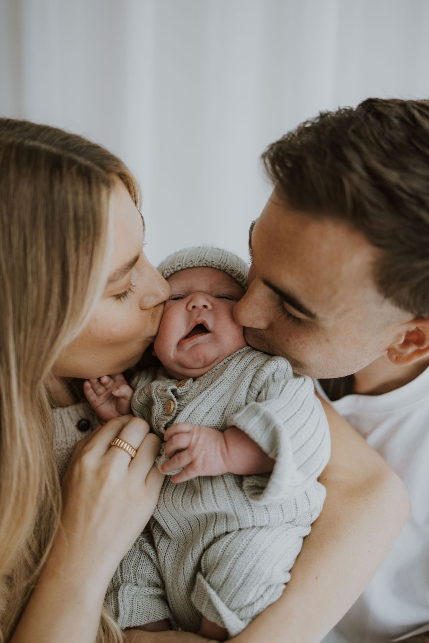 Parents kissing their baby's cheeks in intimate family portrait.